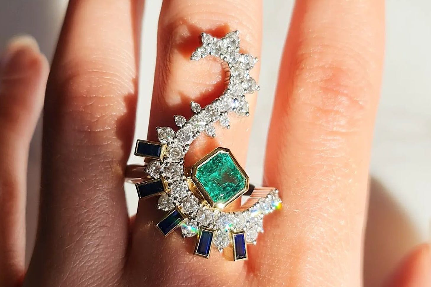 Someone wears an incredible s-shaped diamond and emerald ring.